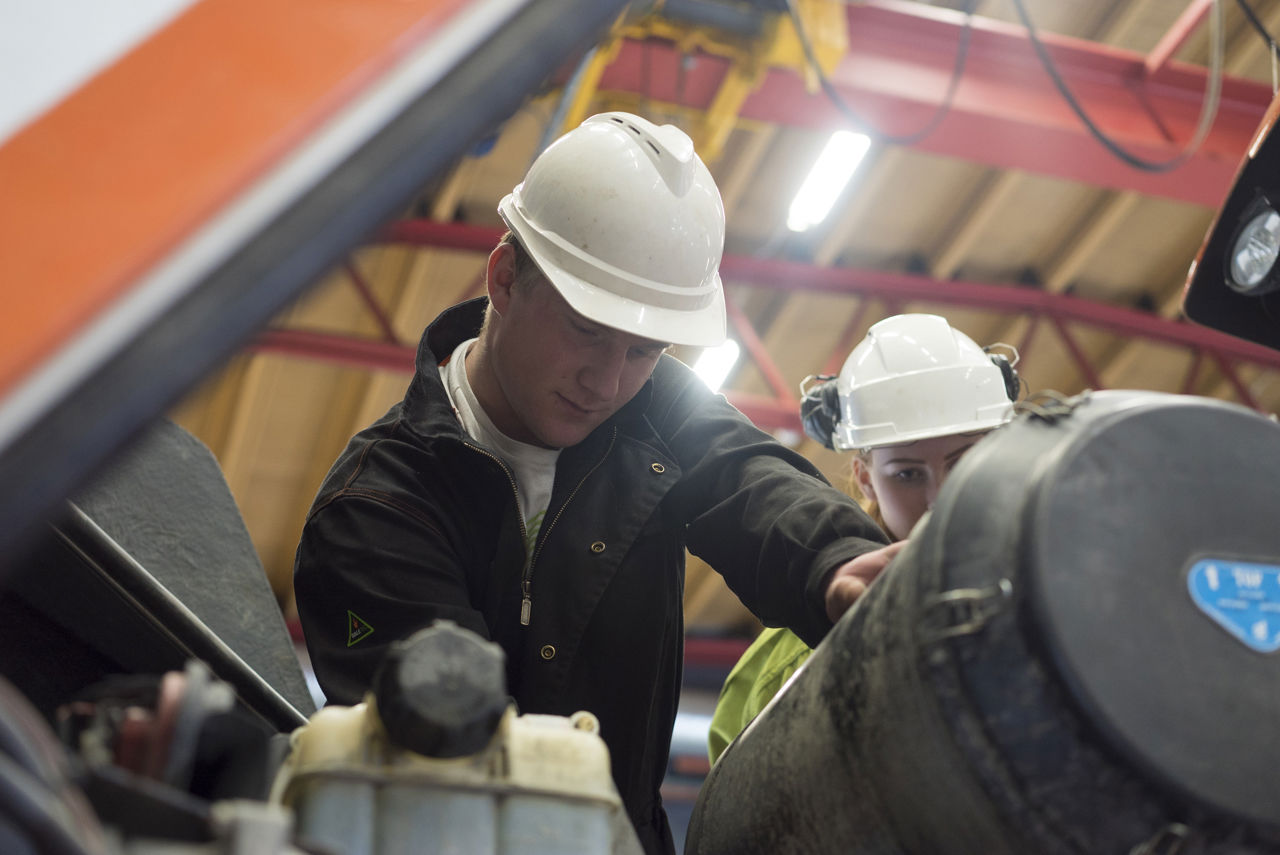Bilete av mekanikar som jobbar med motor og girkasse i verkstad.